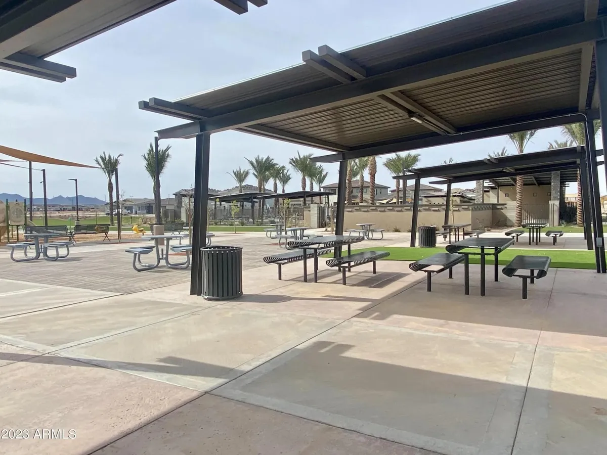 A landscaped outdoor area featuring picnic tables under modern shade structures, surrounded by palm trees and greenery. The space is designed for community gatherings, outdoor dining, and recreational activities, giving an inviting sense of neighborhood life and relaxation.