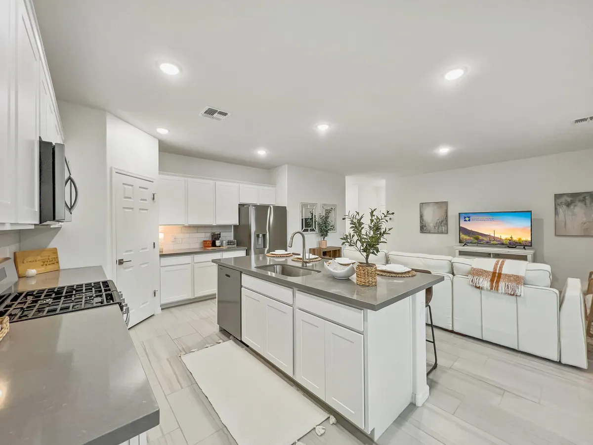A modern kitchen and living area with a central island, stylish seating, high-end appliances, and a television visible in the background. The space looks contemporary and inviting, ideal for meals, entertaining, or relaxing.