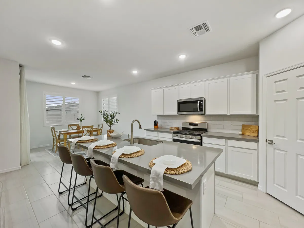 An inviting view of the kitchen and dining area, with a kitchen island, set dining table, and decorative plant. The arrangement hints at shared meals, celebrations, and lively conversations in a cohesive, communal atmosphere.