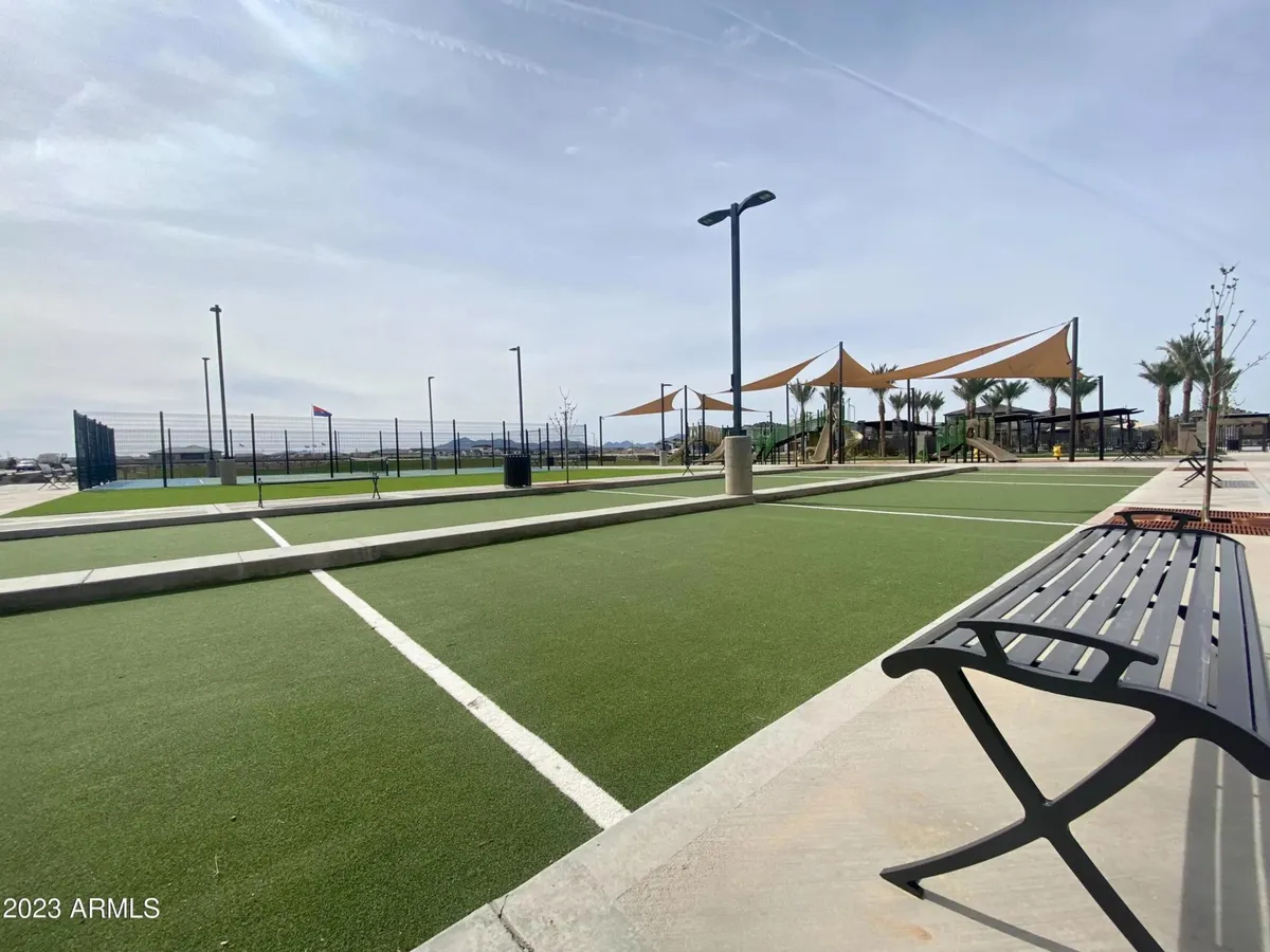 A broad view of a local park area featuring a playground, sports courts, shaded benches, and walking paths. Families are engaged in various activities including playing, picnicking, and light sports. The scene conveys a sense of joyful community and multiple recreational options.