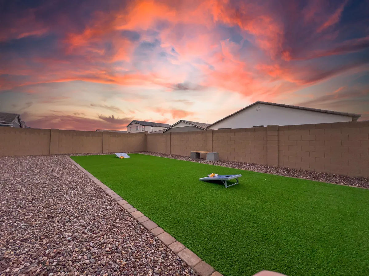 A beautifully manicured green lawn at sunset, with a cornhole game set up and a peaceful sky. The setting is relaxed, suggesting friendly competition and family enjoyment in a safe, outdoor environment.