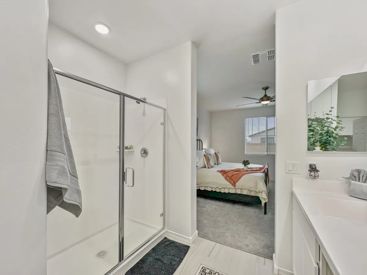 A calming bathroom scene that includes a modern shower area, sleek vanity, and a glimpse of the connected bedroom through an open doorway. The overall ambiance is soothing, with fresh, minimal decor.