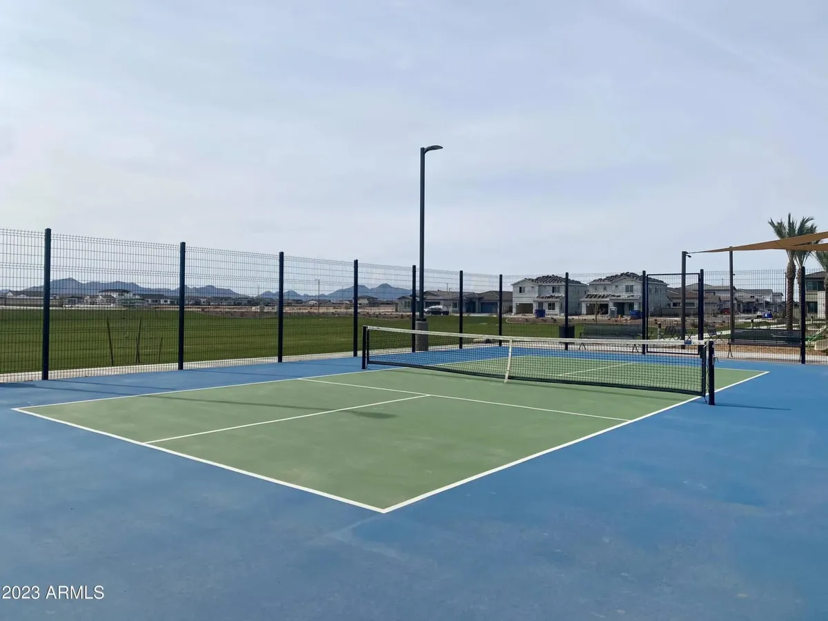This image presents an exterior view of a vibrant tennis court set against a scenic landscape. The court is ready for play with a net strung up, inviting guests to engage in friendly matches or energetic games. The surrounding outdoor setting hints at resort-style amenities and provides a sense of space for group activities.