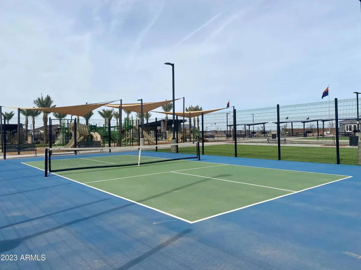 This image captures a vibrant community setting with a tennis court, palm trees, and playground equipment. The area is lively, suggesting opportunities for tennis matches, family gatherings, and children playing, all within a landscaped park-like setting.